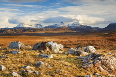 Striking boulders in the wintry Scottish Highlands with the snow-capped mountains of Suilven and Stack Polly in the background