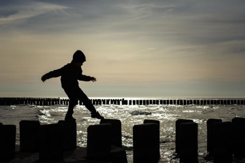 Symbolic photo on the theme of children's courage. A child balances on wooden stilts over the water. Arenshoop