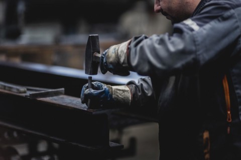 A metal worker marks a drill hole on a steel beam