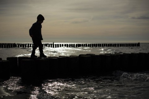 Symbolic photo on the subject of children's fear. A child balances on wooden stilts over the water. Arenshoop