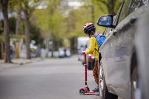 Symbolic photo on the subject of children in road traffic A little boy stands with his scooter between parked cars on a street. Berlin