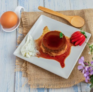 Egg custard with cream and strawberries on a white plate on a blue wooden table with flowers