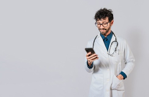 Smiling doctor using cellphone isolated. Young doctor with phone isolated