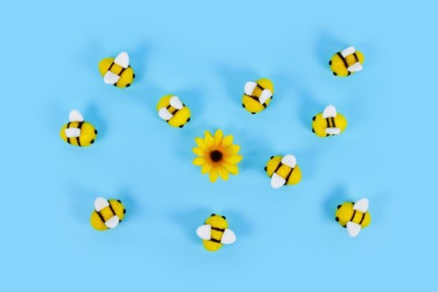 Cute felt bees surrounding yellow flower on blue background
