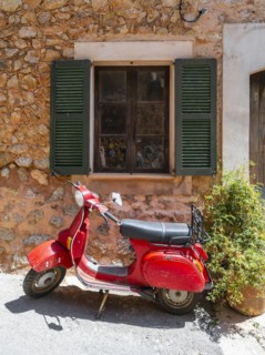 Red Vespa in front of the window of a typical stone house