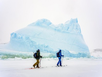 Ski tourers in front of iceberg in frozen Kong Oscar Fjord