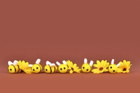 Felt bees and yellow flowers in a row on brown background with copy space