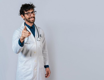 Smiling doctor pointing at you isolated. Young doctor pointing at you. Friendly doctor pointing at the camera
