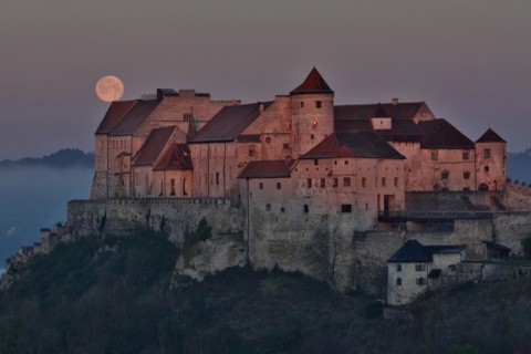 The full moon sets behind the castle in Burghausen