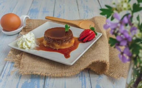 Egg custard with cream and strawberries on a white plate on a blue wooden table with flowers