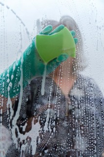Closeup of a woman cleaning the windows of her house with a green rag and rubber gloves