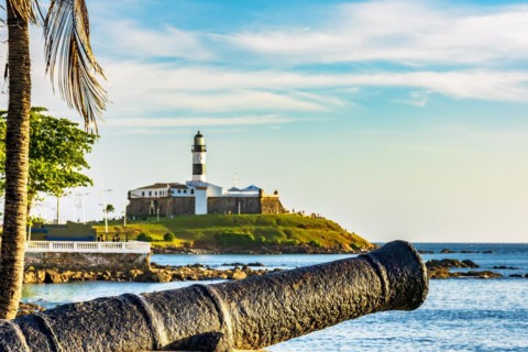Old cannon and the Barra Lighthouse one of the main historical buildings and tourist spot in the city of Salvador in Bahia surrounded by the sea during the late afternoon.