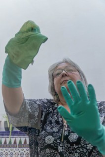 Closeup of a woman cleaning the windows of her house with a green rag and rubber gloves