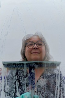 Close-up of a white-haired woman cleaning soap-covered windows with a squeegee