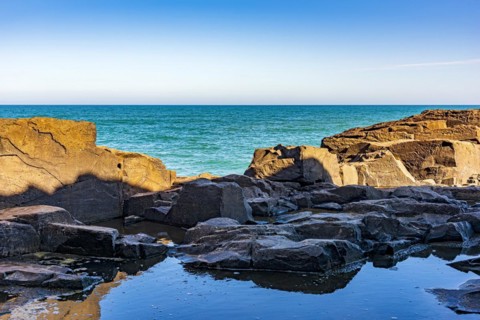 Rock formation in front of the sea and the horizon in a blue sky afternoon in Torres city