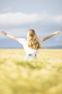 A young girl walks through a cornfield on a sunny warm day and spreads out her arms