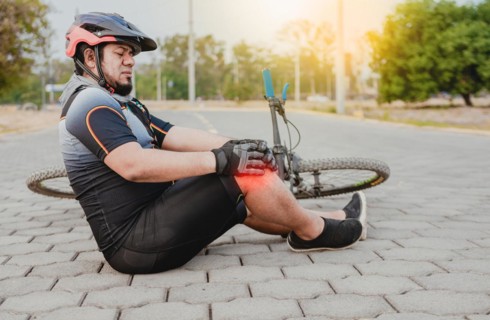 Cyclist with knee pain outdoors. Male cyclist sitting on the pavement with knee pain. Concept of a cyclist with knee injury outdoors