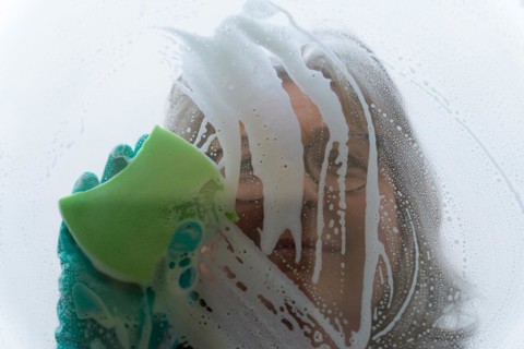 Closeup a woman cleans the glass with a green sponge and gloves