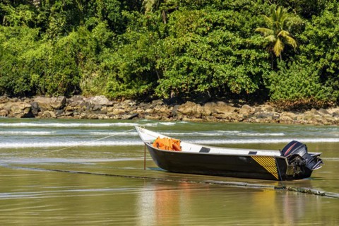 Speedboat standing on the sand of the beach with the rocks and rainforest in the background on a sunny day in Bertioga on the coast of the state of Sao Paulo