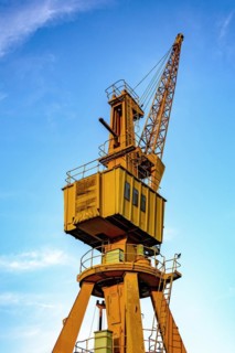 Old and obsolete yellow crane on the harbor pier with blue sky in the background.