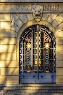 Old and imposing metal gate decorated with golden details with shadows and reflections of the late afternoon sun