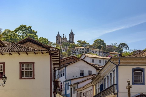 Facade of colonial-style houses in the historic city of Ouro Preto in Minas Gerais with a baroque church on top of the hill in the background.