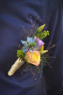 Close up of flower clip called 'boutonniere' for groom attached to pocket of dark blue shirt made from beautiful natural roses and wild flowers