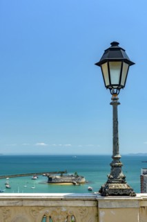 Old lamppost on a wall overlooking the sea and historic fortification in Todos os Santos Bay in Salvador