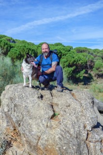 Man on a rock with his border collie dog with a pine forest in the background