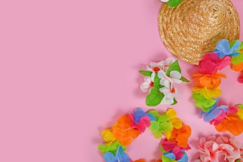 Bright flower lei necklaces and summer straw hat on side of pink background with copy space