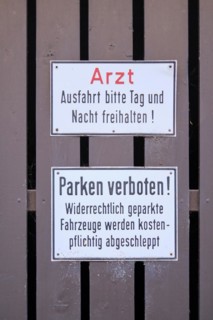 Signs doctor. Exit please keep clear day and night! and Parking prohibited! Illegally parked vehicles will be towed away for a fee mounted on brown painted wooden slats