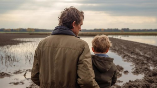 Distressed farming father and son look over their flooded farmland