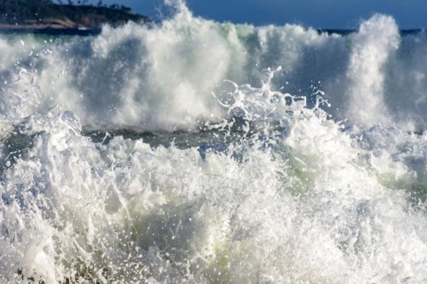 Colorful sea waves crashing on the beach on a sunny summer day with water drops and foam splashing in the air