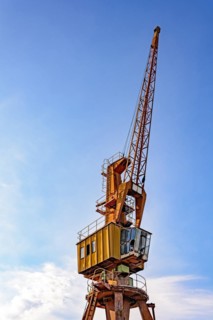 Old and obsolete yellow crane on the harbor pier with blue sky and clouds in the background.