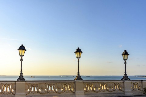 Old colonial style lanterns lighting on walls in the streets of Salvador with the All Saints bay in the background with their boats during the sunset