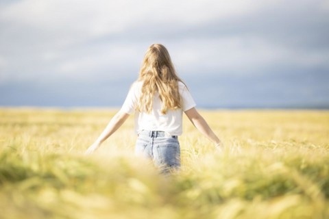 A young girl walks through a cornfield on a sunny warm day and spreads out her arms