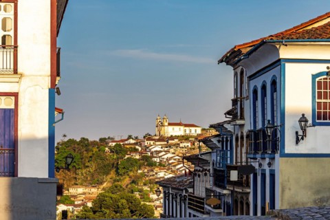 Streets and houses in the historic city of Ouro Preto in Minas Gerais with a church on top of the hill in the background.