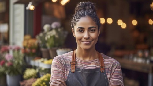 Proud young adult multi-ethnic female at the entrance of her quaint flower shop in europe