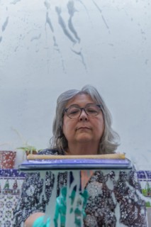 Close-up of a white-haired woman cleaning soap-covered windows with a squeegee