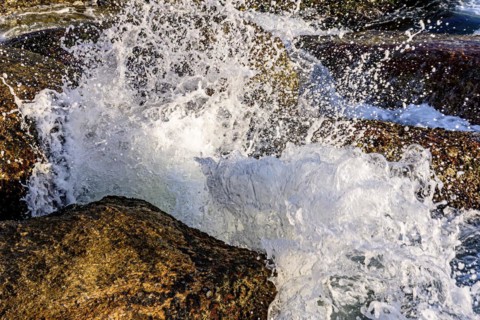 Water and sea foam splashing in the air with waves crashing against rocks