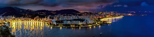 Panoramic photograph of the shore of Guanabara Bay in Rio de Janeiro at night with the buildings and citylights in Botafogo and Flamengo neighborhoods and the hills in the background