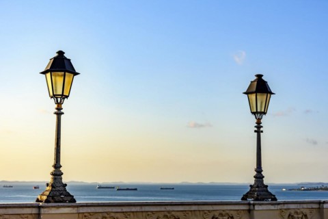 Old lanterns lighting on walls in the streets of Salvador with the All Saints bay in the background with their boats during the sunset