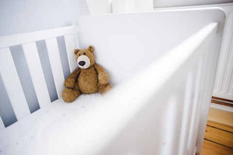 Symbolic photo on the subject of wanting a child. A teddy bear sits in an empty cot. Berlin