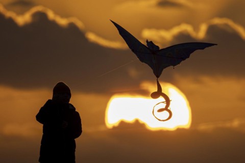 A silhouette of a child flying a kite in front of the sunset in Berlin