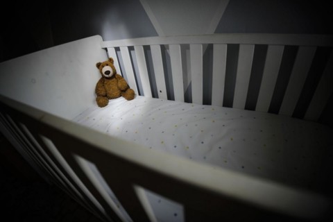 Symbolic photo on the subject of child abuse. A teddy bear sits in an empty cot. Berlin