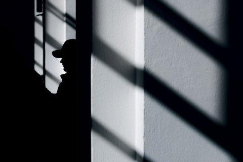 Symbolic photo on the subject of male criminality. The silhouette of a man wearing a baseball cap stands out between shadows of a window.Berlin