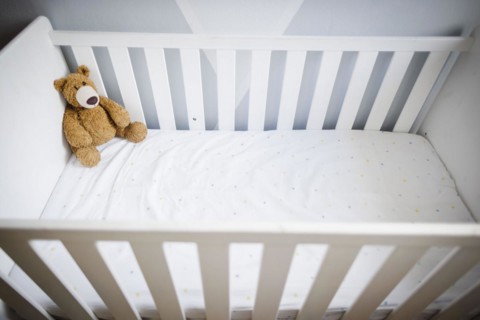 Symbolic photo on the subject of wanting a child. A teddy bear sits in an empty cot. Berlin