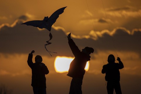 The silhouette of three people emerges while flying a kite in front of sunset in Berlin