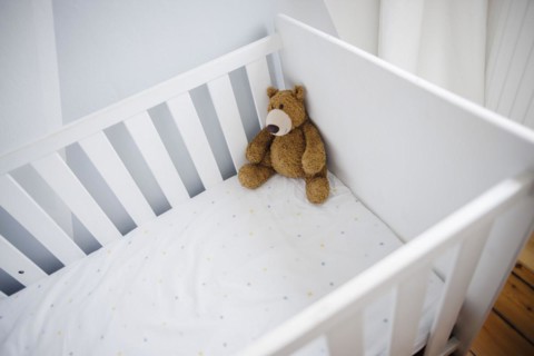 Symbolic photo on the subject of wanting a child. A teddy bear sits in an empty cot. Berlin