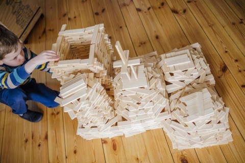 Symbolic photo on the subject of creative play among children. A boy builds with wooden building blocks. Berlin